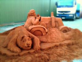 Sand sculpture of bear and tractor.